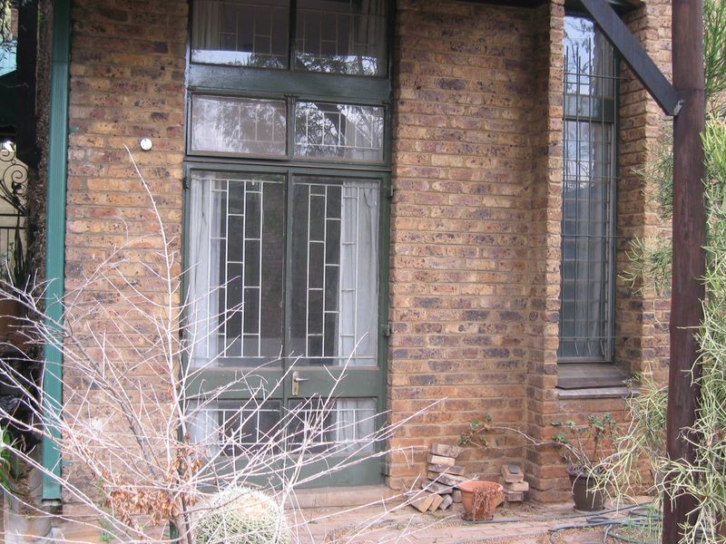 Rear exterior view of a townhouse featuring a face brick facade, security-fitted timber glass doors, and a paved patio area.