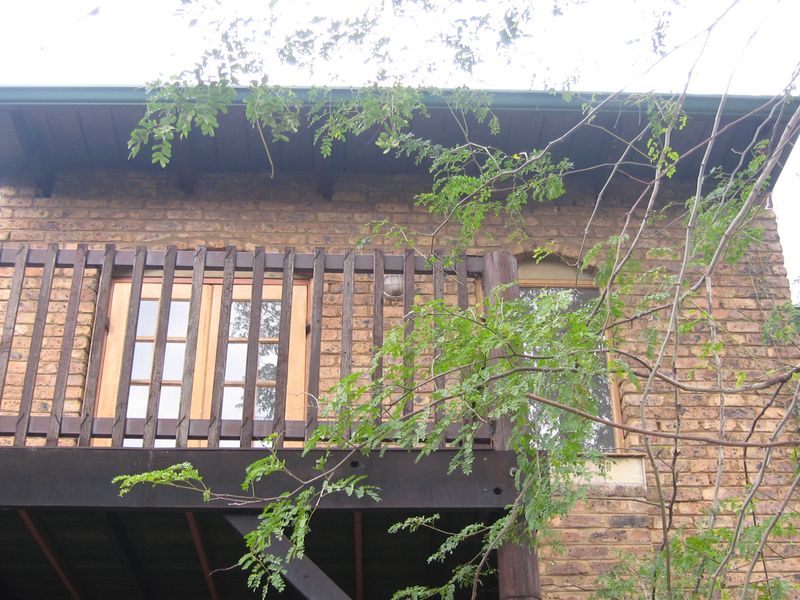 An elevated timber balcony featuring brick facade walls and wooden french doors, showing signs of weathered timber finishes.