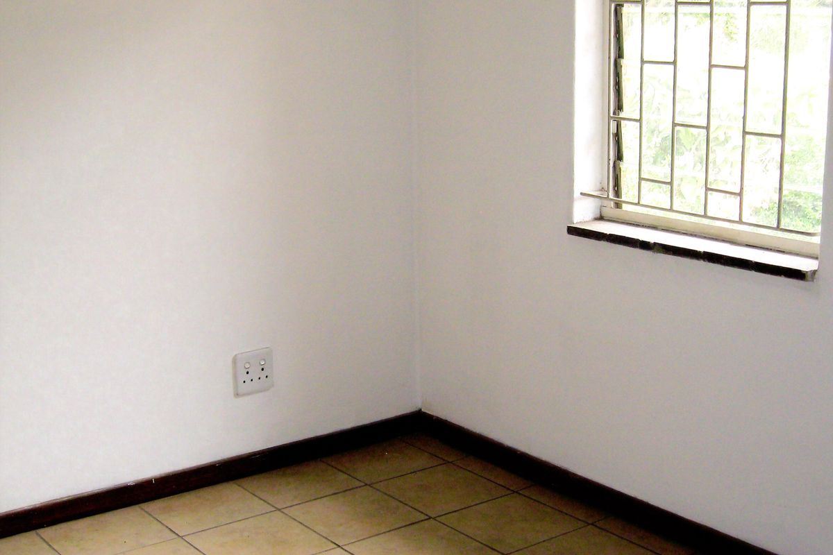 A vacant bedroom featuring tiled flooring, white walls, and a window fitted with security bars.