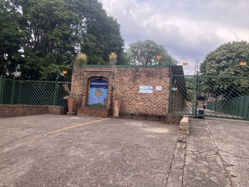 Front entrance view of the townhouse complex featuring a brick boundary wall, electric fencing, and a secure metal gate entrance.
