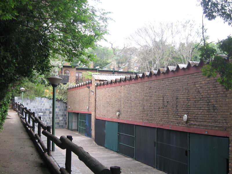 A view of a row of garages with brick walls and paved access path, featuring a timber safety railing and exterior lighting.