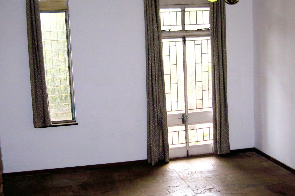 An empty living room featuring stone tile flooring, large windows with security bars, and a glass-paneled door leading to the exterior.