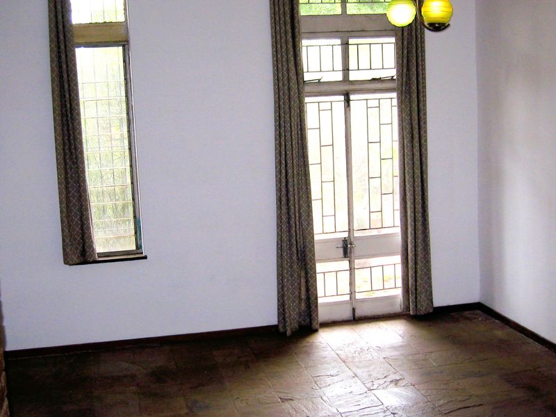 An empty living room featuring stone tile flooring, large windows with security bars, and a glass-paneled door leading to the exterior.