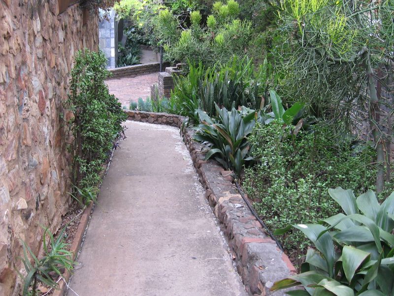 A landscaped garden pathway featuring a concrete walkway bordered by stone retaining walls and established greenery.