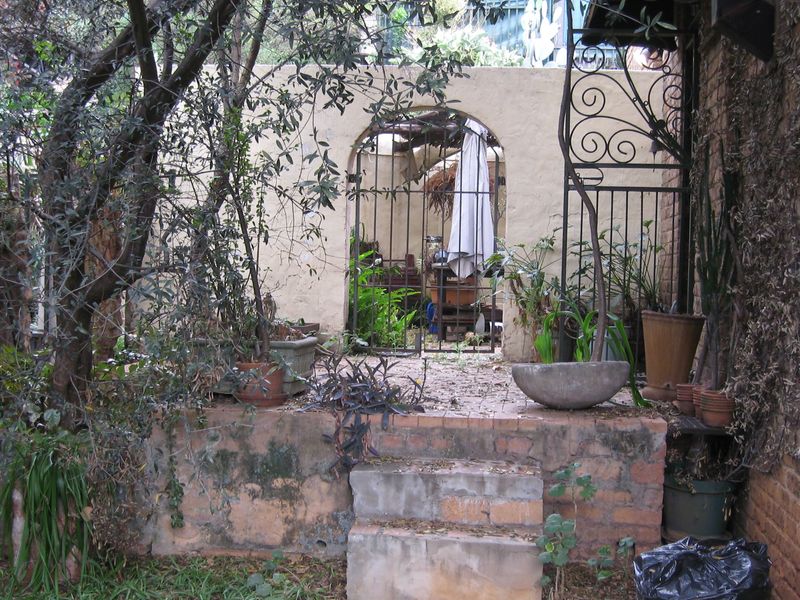 A weathered outdoor patio area featuring brick steps, an arched masonry wall, and a decorative wrought iron gate, offering potential for garden landscaping.