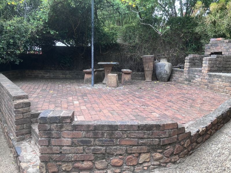Outdoor patio area featuring rustic brick paving, a built-in brick braai, and low brick retaining walls, set within a garden environment.