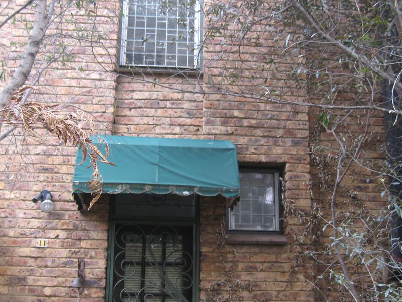 Front entrance of a brick townhouse featuring a security gate, window security bars, and a green fabric awning.