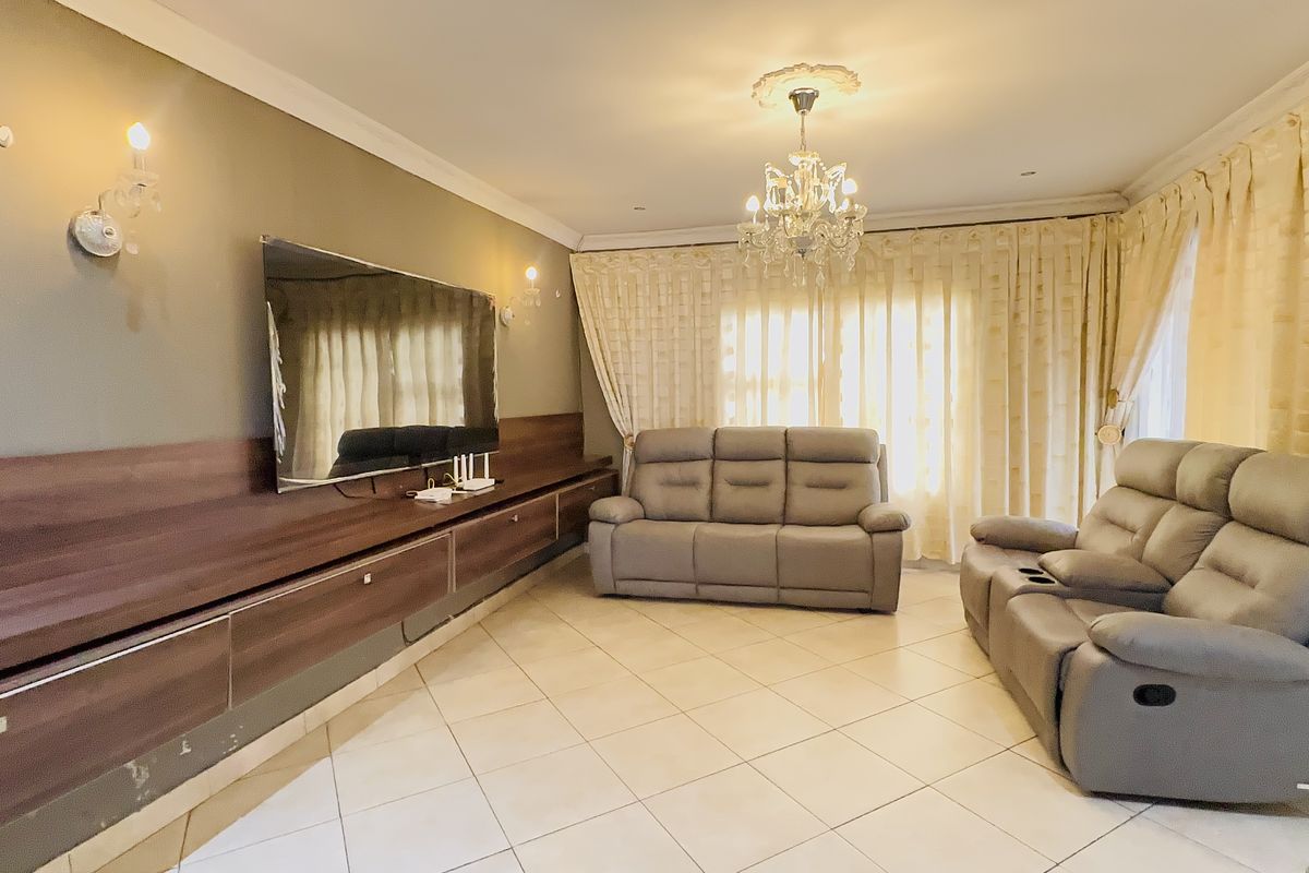 A spacious living room featuring tiled flooring, a large built-in media unit, decorative ceiling rose with chandelier, and elegant wall sconces.