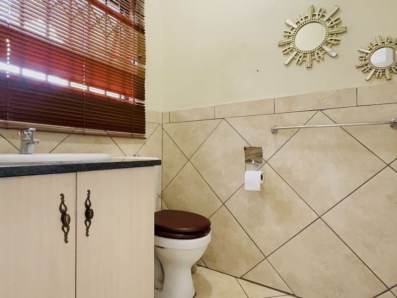 A functional bathroom featuring a vanity cabinet with basin, toilet, and neutral diamond-patterned wall tiling.