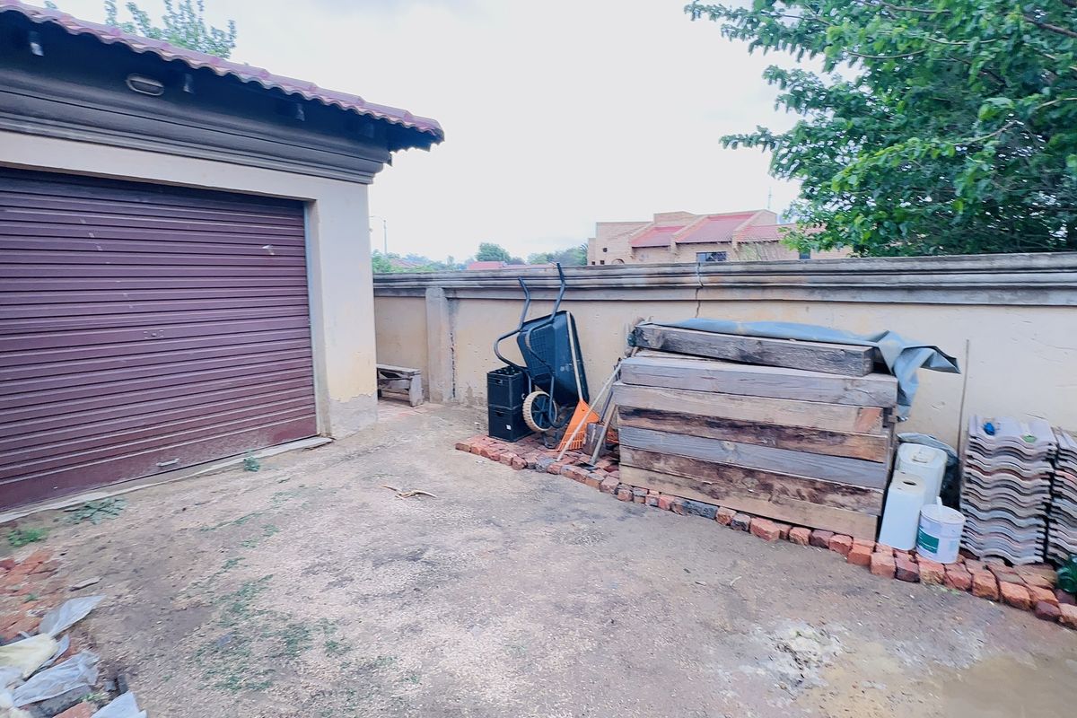 Rear exterior area featuring a roller garage door and perimeter boundary wall, requiring maintenance and landscaping to improve the outdoor space.