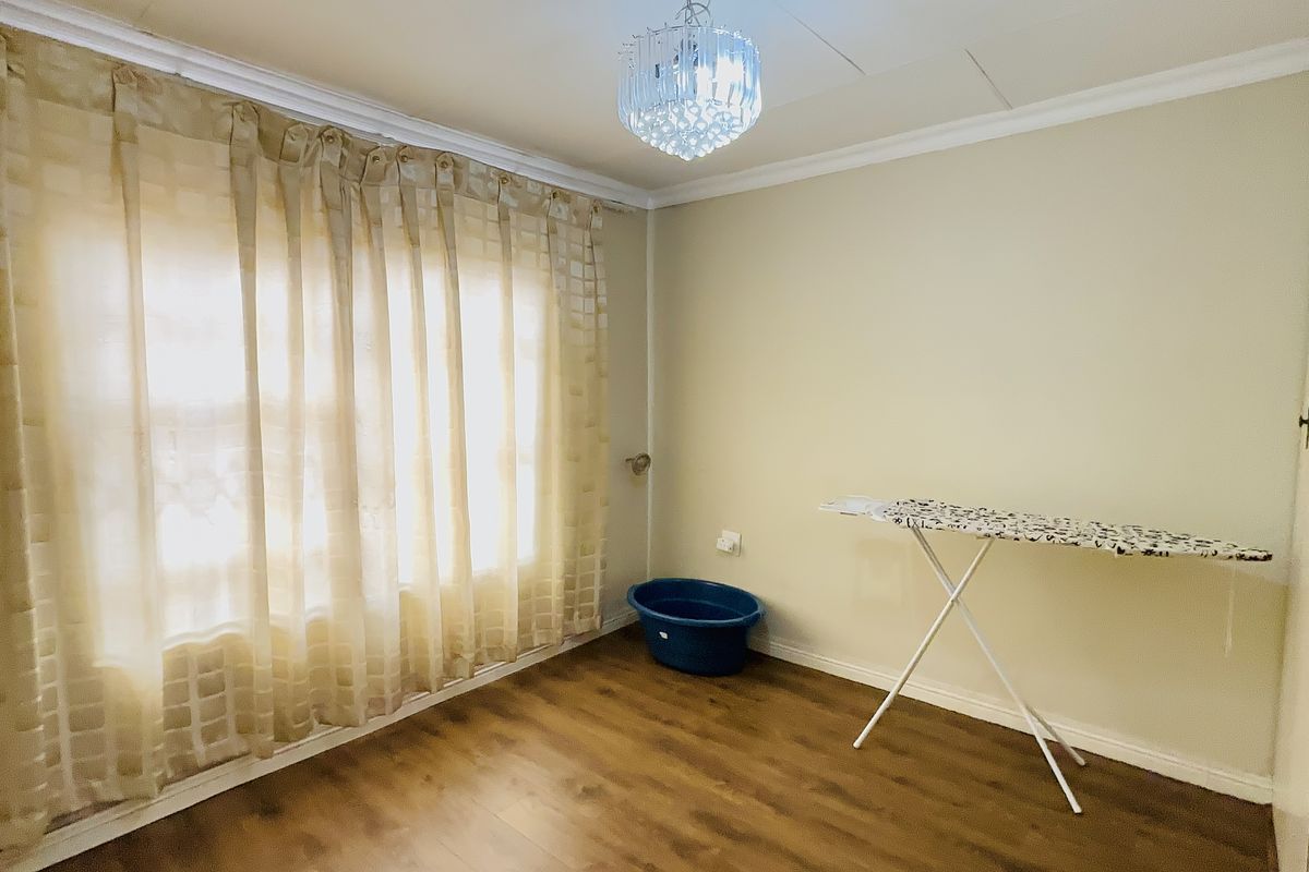 A bright, empty bedroom featuring laminate flooring, crown molding, and a decorative crystal chandelier.