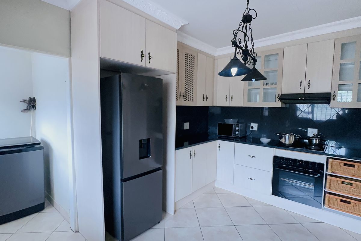 A functional kitchen featuring light-toned cabinetry, black granite countertops, built-in oven, extractor fan, and tiled flooring with an adjacent laundry area.