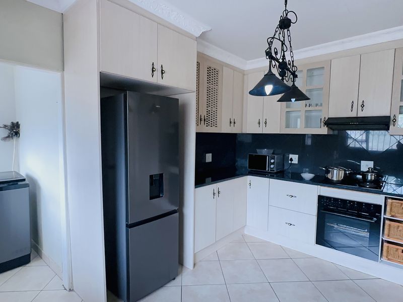 A functional kitchen featuring light-toned cabinetry, black granite countertops, built-in oven, extractor fan, and tiled flooring with an adjacent laundry area.