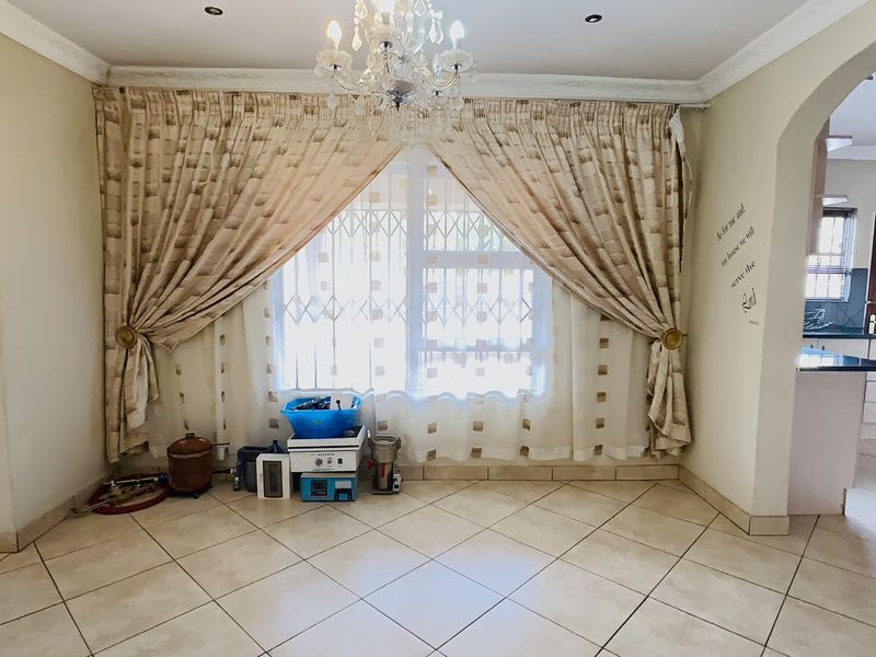 A bright, open-plan living area featuring neutral tiled flooring, a decorative chandelier, and an arched entryway leading to the kitchen.