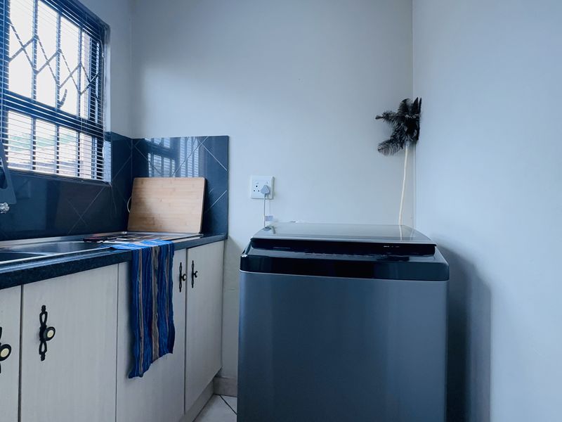 A functional laundry area featuring built-in cabinetry, a stainless steel sink with tiled splashback, and space for a washing machine.
