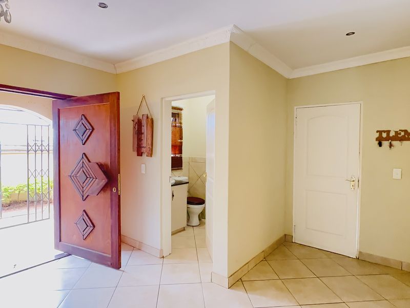 A bright entrance hall featuring tiled flooring, a decorative solid wood front door, and access to an adjacent guest bathroom.