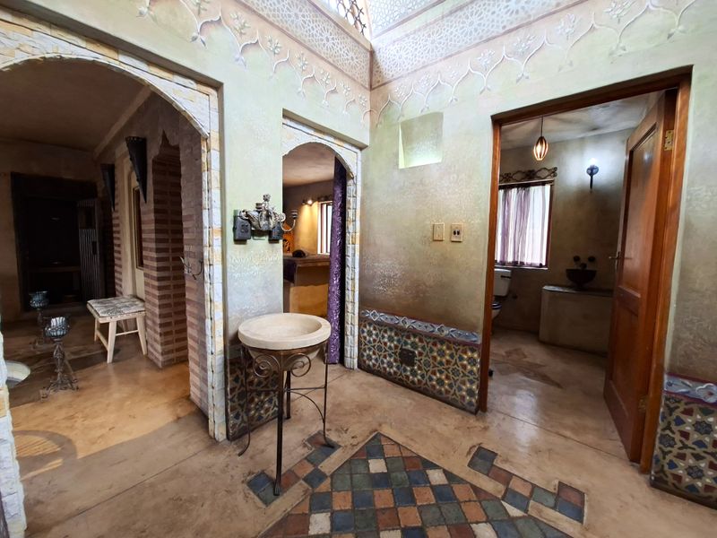 A unique hallway featuring decorative wall tiling, arched architectural details, a stone basin, and a skylight providing natural illumination.