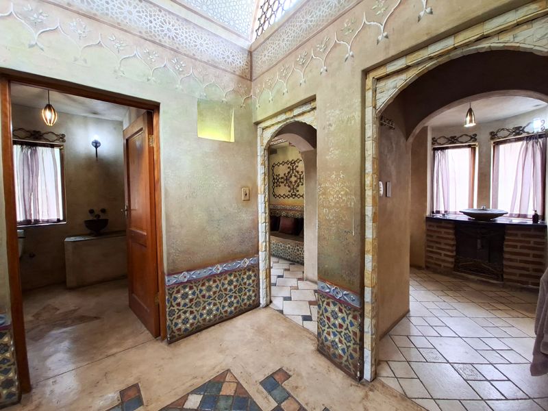 A unique hallway featuring intricate decorative wall finishes, arched architectural transitions, tiled flooring, and a skylight providing natural illumination to the connecting spaces.