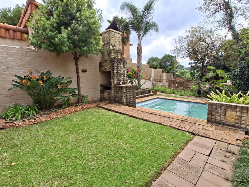 Outdoor entertainment area featuring a swimming pool, built-in braai, and landscaped garden with brick paving.
