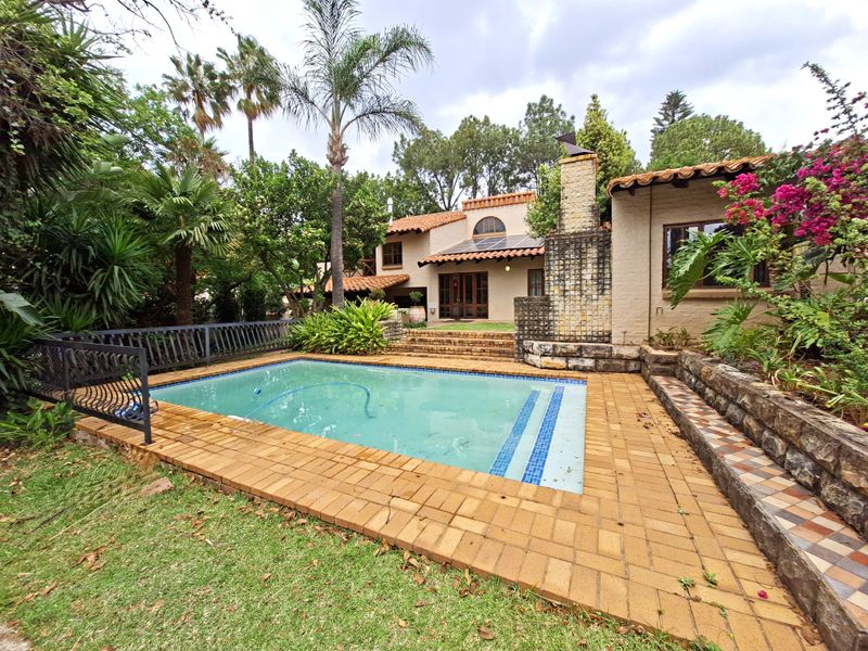 A private outdoor pool area featuring brick paving, a stone retaining wall, and an integrated outdoor fireplace set against a landscaped garden.