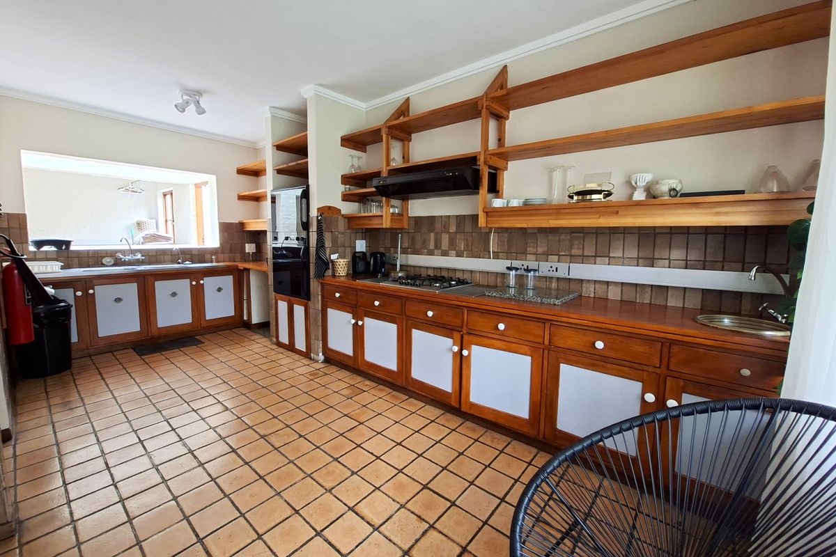 A spacious kitchen featuring extensive wooden cabinetry, open shelving, tiled flooring, a gas hob with extractor, and a double sink setup.
