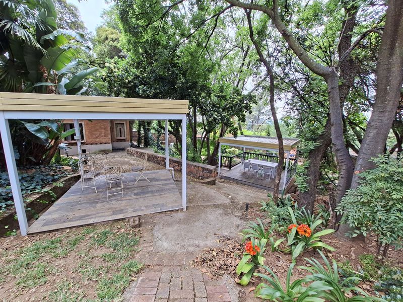 A lush, tiered garden featuring multiple timber-decked patio areas, stone retaining walls, and mature trees providing a serene outdoor entertainment space.
