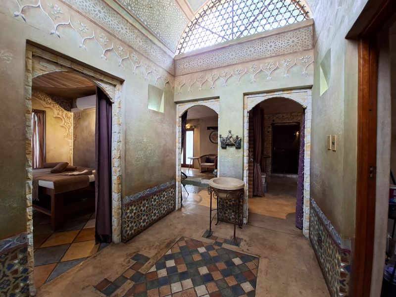 A uniquely designed hallway featuring intricate wall plastering, arched doorways, a vaulted ceiling with decorative lattice, and detailed tiled floor accents.