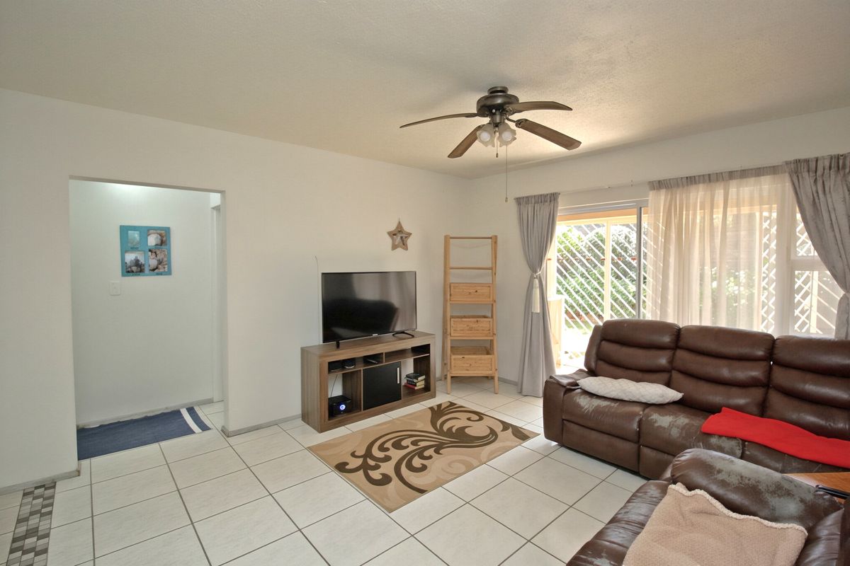 A living room featuring tiled flooring, a ceiling fan, and a sliding glass door providing access to the outdoor area.