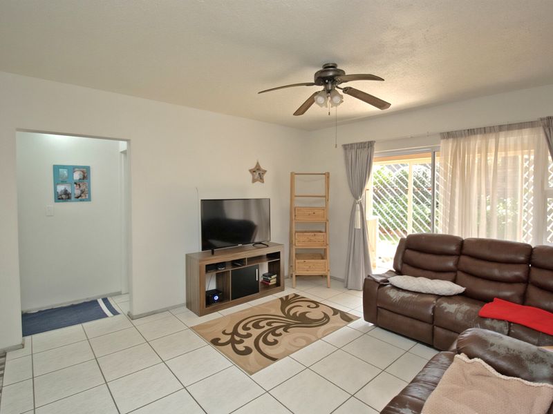 A living room featuring tiled flooring, a ceiling fan, and a sliding glass door providing access to the outdoor area.