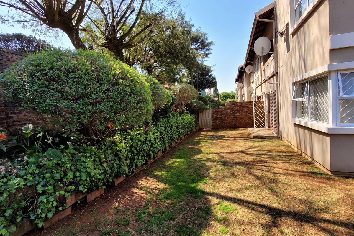 A private rear garden area featuring a brick boundary wall, established hedge, and direct access to the townhouse exterior.
