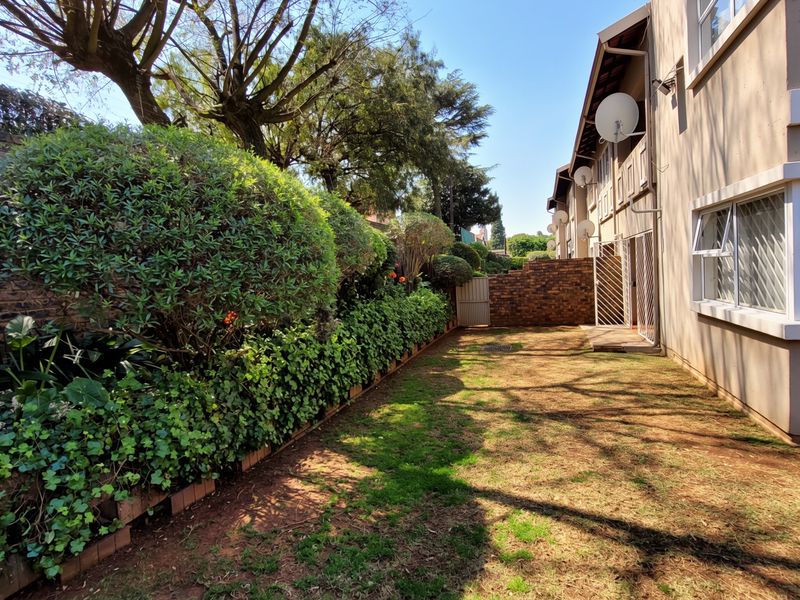 A private rear garden area featuring a brick boundary wall, established hedge, and direct access to the townhouse exterior.
