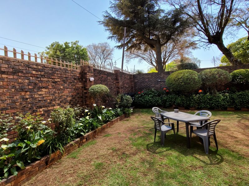 A private rear garden featuring a well-maintained lawn, established garden beds with brick edging, and a secure face brick boundary wall with electric fencing.