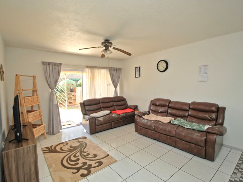 A living room featuring ceramic tile flooring, a ceiling fan, and a sliding glass door providing access to the outdoor area.