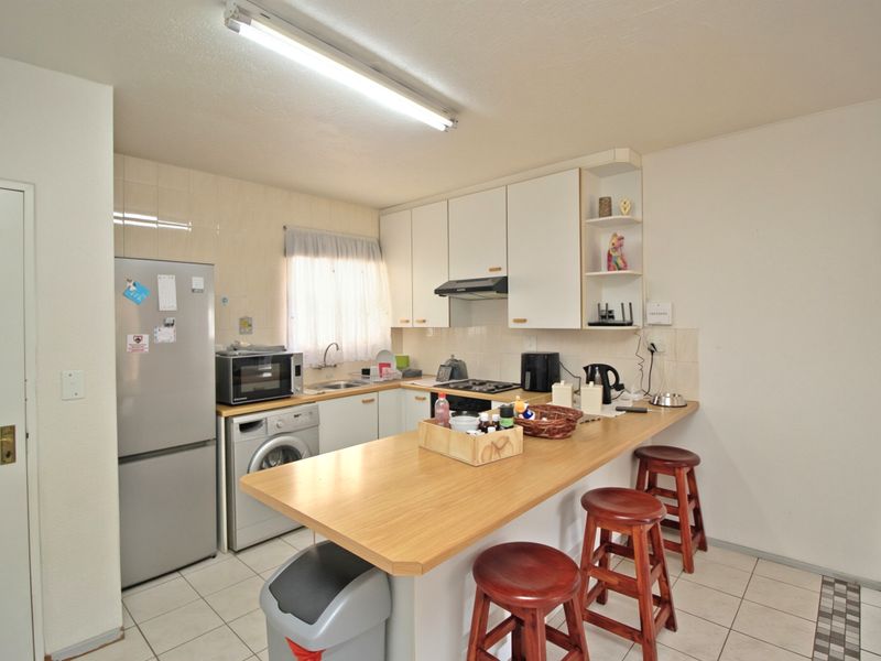A functional kitchen featuring white cabinetry, a breakfast bar with wood-look countertop, tiled backsplash, and integrated hob with extractor fan.