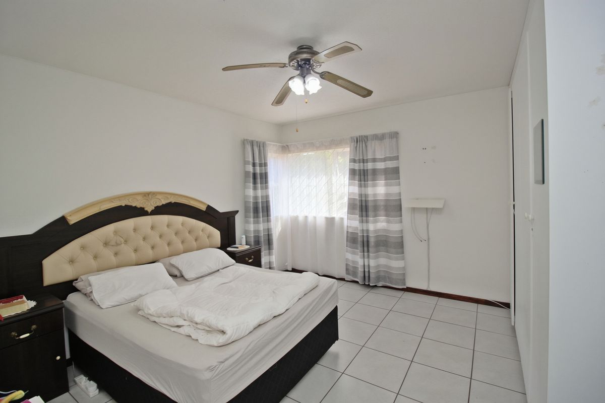 A bedroom featuring tiled flooring, a ceiling fan, and built-in cupboards, offering a functional space with potential for cosmetic updates.
