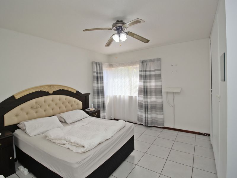 A bedroom featuring tiled flooring, a ceiling fan, and built-in cupboards, offering a functional space with potential for cosmetic updates.