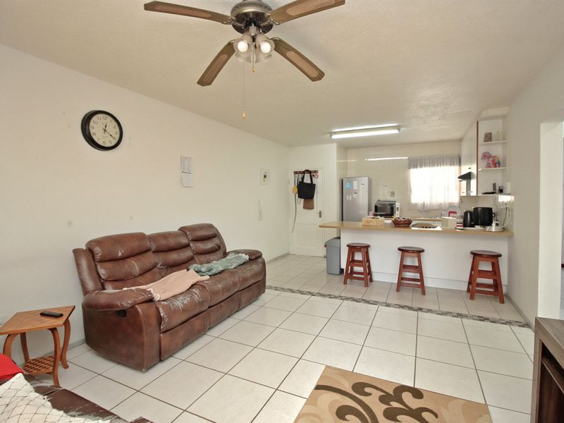 Open-plan living and kitchen area featuring tiled flooring, a breakfast bar, and a ceiling fan, offering a functional layout for daily living.