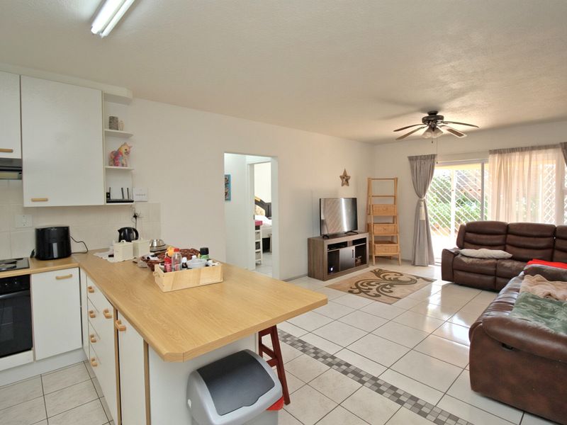 Open-plan living area featuring a functional kitchen with built-in cabinetry and appliances, flowing into a bright lounge space with direct access to the outdoors.