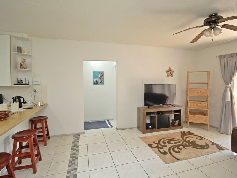 Open plan living area featuring tiled flooring, a ceiling fan, and a built-in breakfast bar with integrated shelving.