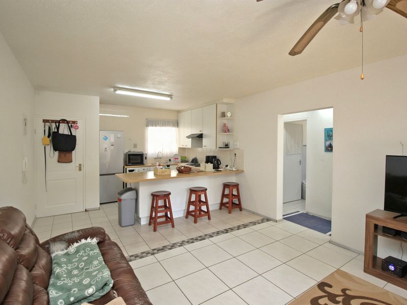 Open plan living area featuring a functional kitchen with breakfast bar, tiled flooring, and a ceiling fan, connecting to adjacent living space.