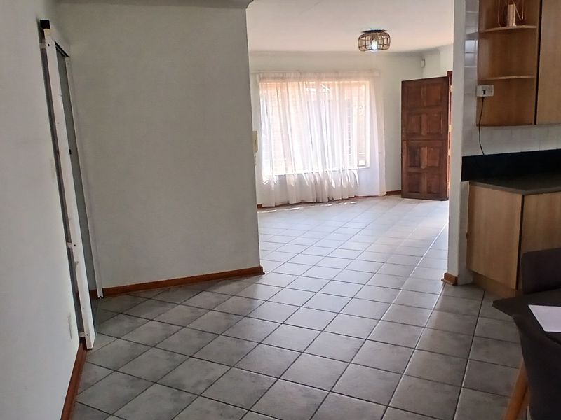 Open plan living area featuring tiled flooring and a functional kitchen with built-in cabinetry, leading to a bright lounge space with natural light.