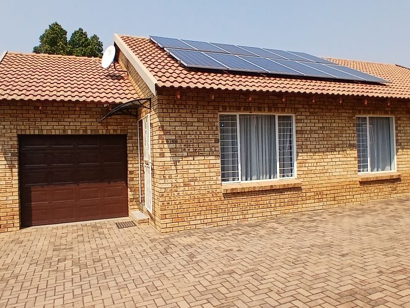 Front elevation of a face-brick cluster home featuring a tiled roof, solar panels, a single garage, and a paved driveway.