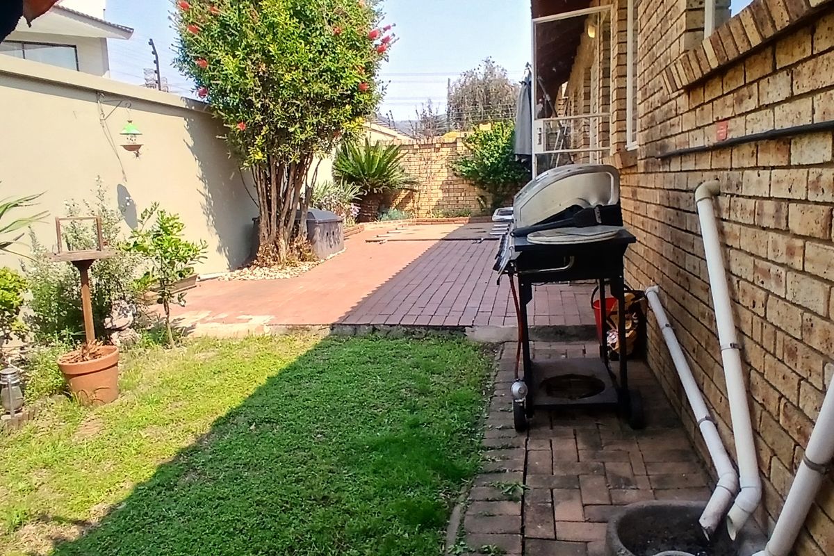 A rear garden area featuring brick paving, a lawn, and a facebrick exterior wall with visible external plumbing.