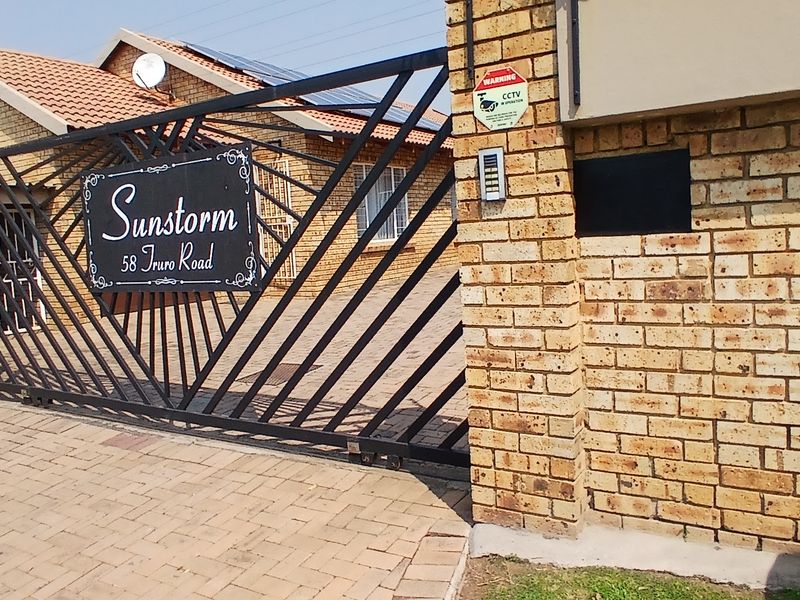 Front entrance view of the cluster complex featuring a secure sliding gate, face brick boundary wall, and paved driveway access.