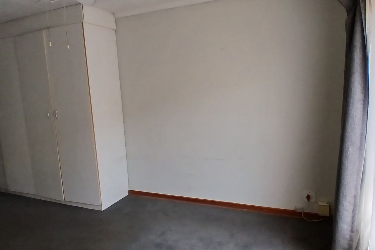A spacious, empty bedroom featuring built-in cupboards, neutral wall finishes, and carpeted flooring, with an adjacent en-suite bathroom visible.