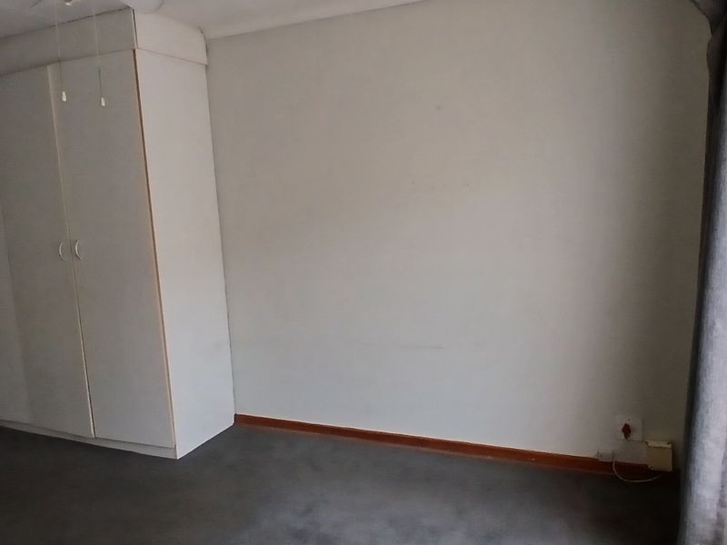 A spacious, empty bedroom featuring built-in cupboards, neutral wall finishes, and carpeted flooring, with an adjacent en-suite bathroom visible.