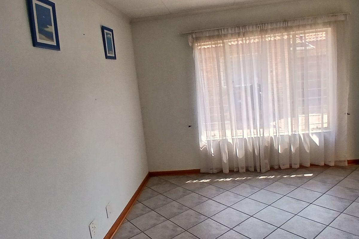 An empty living room featuring tiled flooring, an intercom system, and a window with security bars.