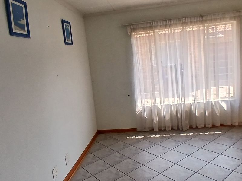 An empty living room featuring tiled flooring, an intercom system, and a window with security bars.