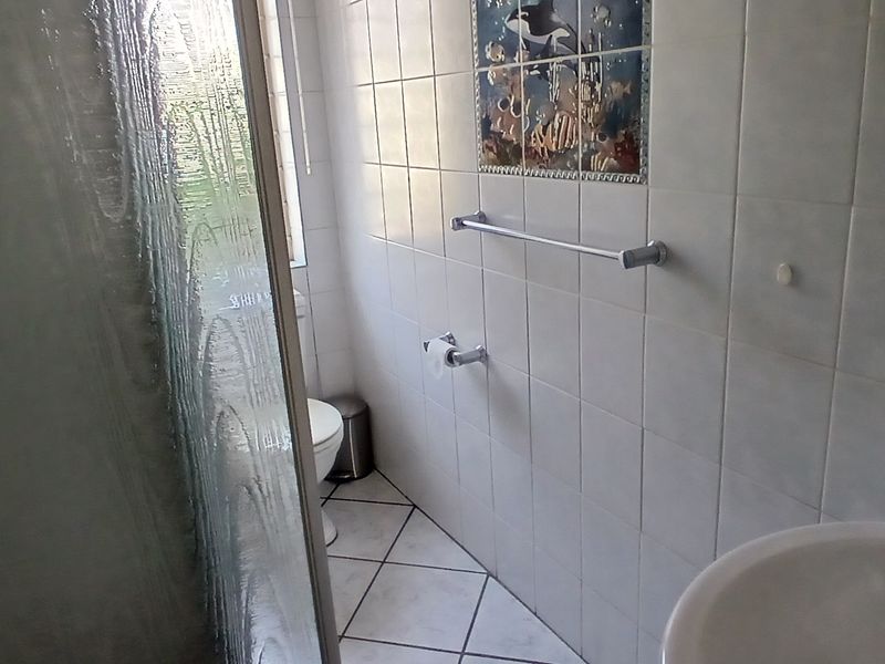 A functional bathroom featuring a shower enclosure, pedestal basin, and toilet with neutral wall and floor tiling.