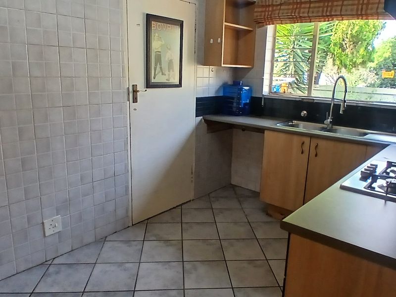 A functional kitchen featuring built-in cabinetry, a gas hob, stainless steel sink, and tiled finishes, offering a practical layout for daily meal preparation.